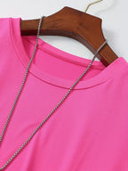 Robe rose vif en tissu léger sur cintre en bois, ornée d'un collier argenté. Mode féminine, vêtement élégant, tendance printemps-été.