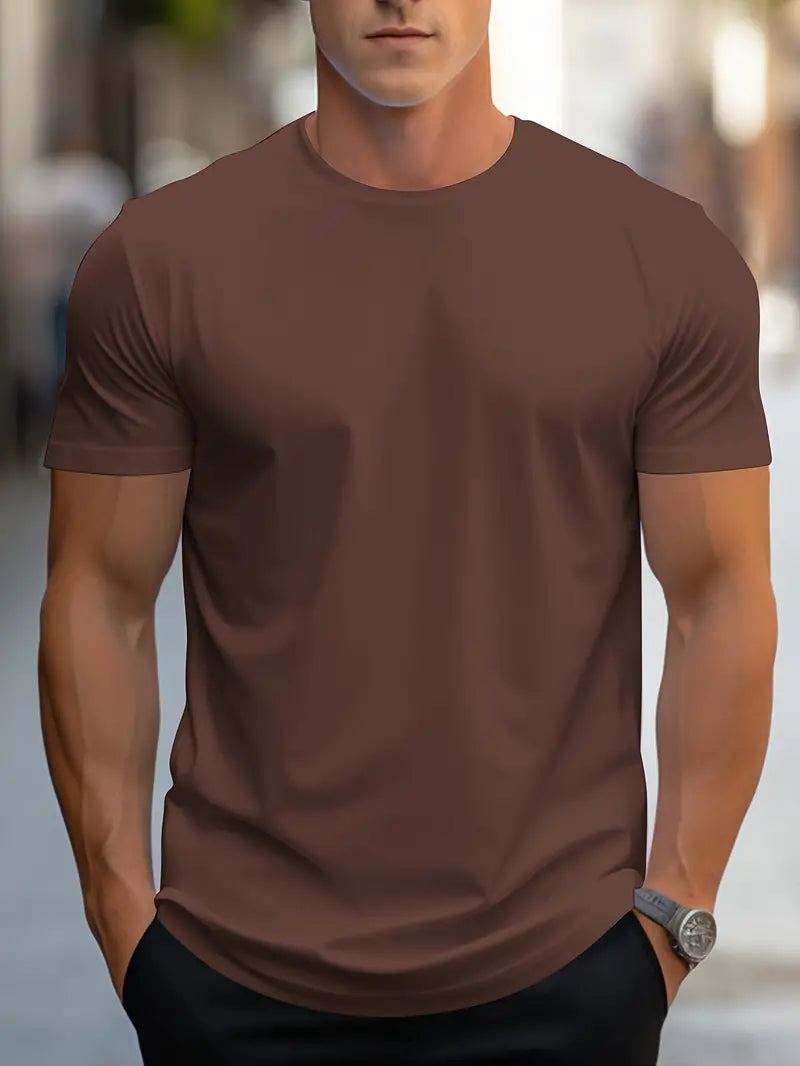 Homme portant un t-shirt marron uni, manches courtes, en extérieur urbain. Mode masculine décontractée, style moderne, montre argentée visible.