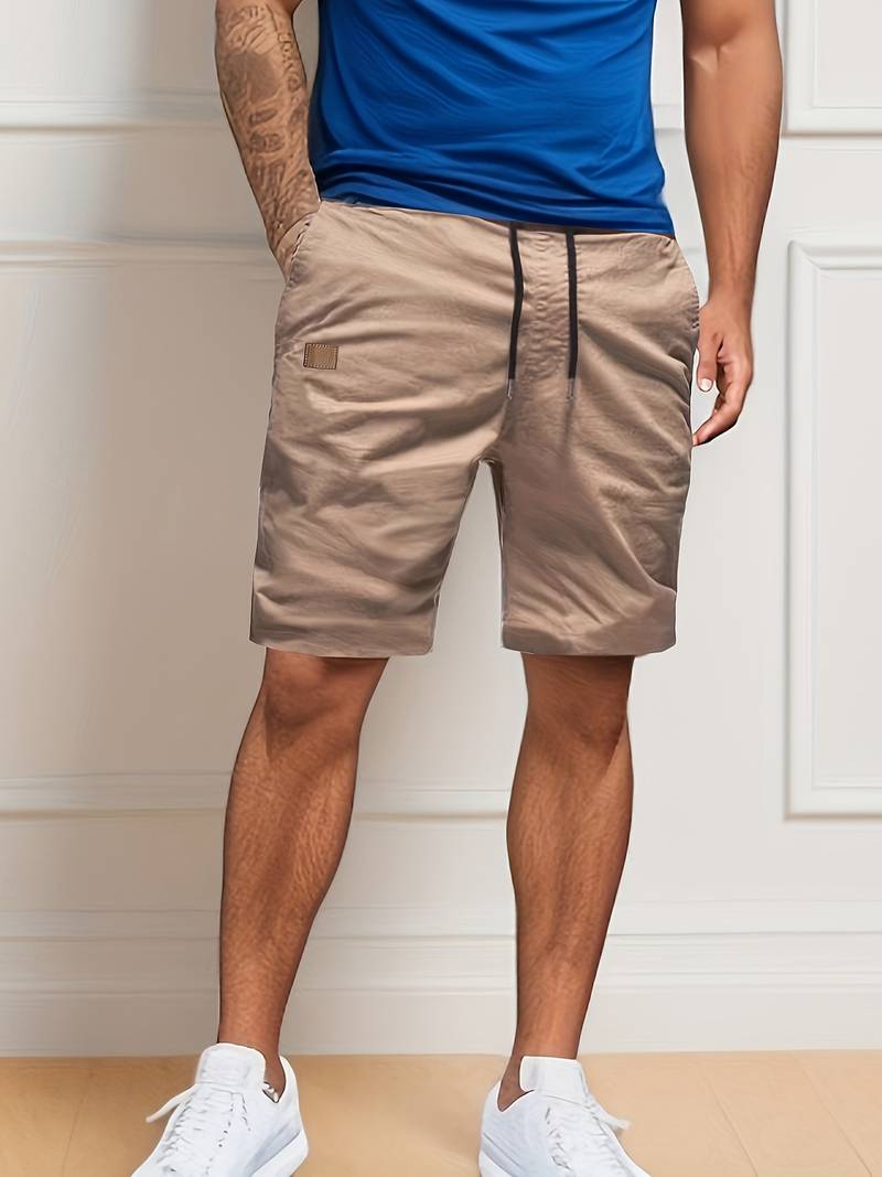 Homme portant un short beige élégant avec cordon, t-shirt bleu et baskets blanches. Mode masculine décontractée, tenue estivale tendance.