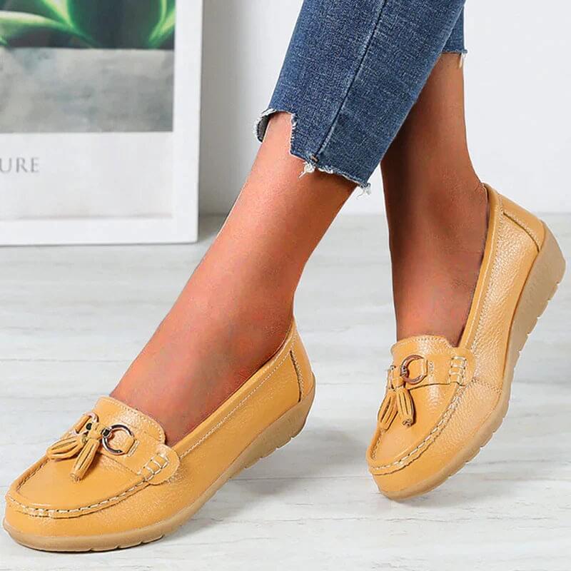 Chaussures mocassins femme en cuir beige avec pompons, portées avec un jean. Confortables et élégantes, idéales pour un style décontracté.