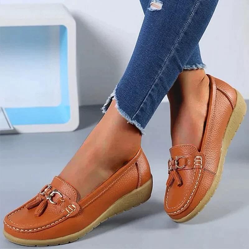 Chaussures mocassins marron pour femme, en cuir, avec semelle compensée beige, ornées de pampilles, portées avec un jean bleu.
