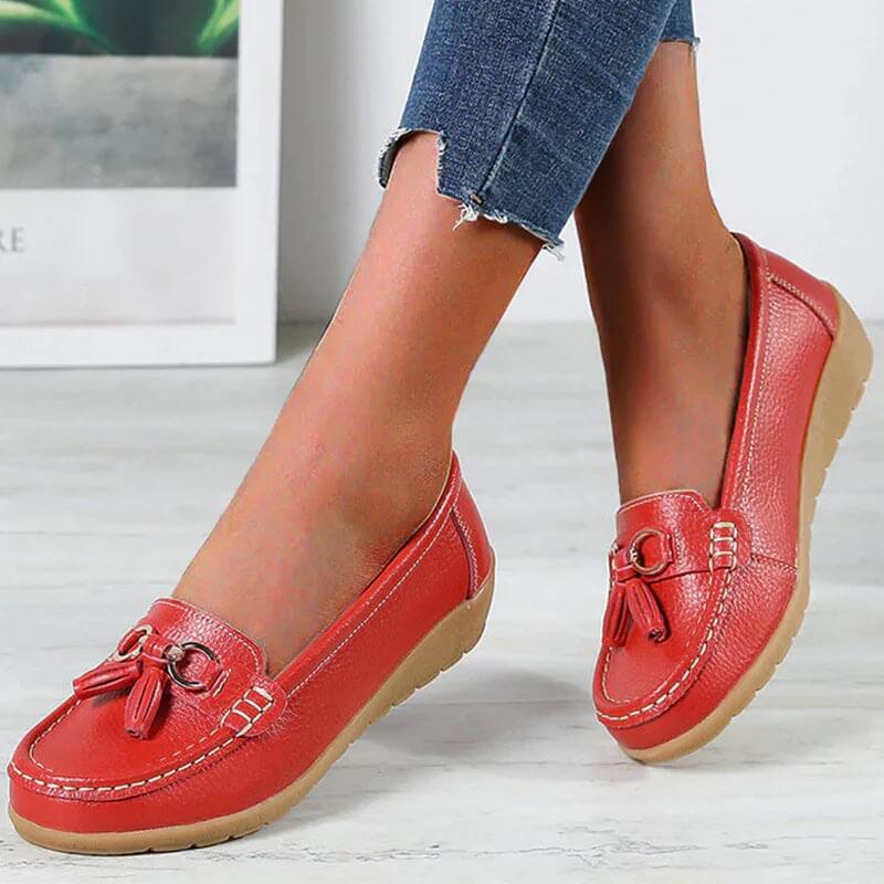 Chaussures mocassins rouges pour femme, en cuir, avec pompons, semelle en caoutchouc beige, portées avec un jean. Mode féminine, confort, style décontracté.