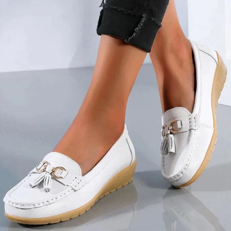 Chaussures mocassins blancs pour femme avec semelle beige, ornées de pampilles, portées avec un pantalon noir. Mode féminine élégante et confortable.