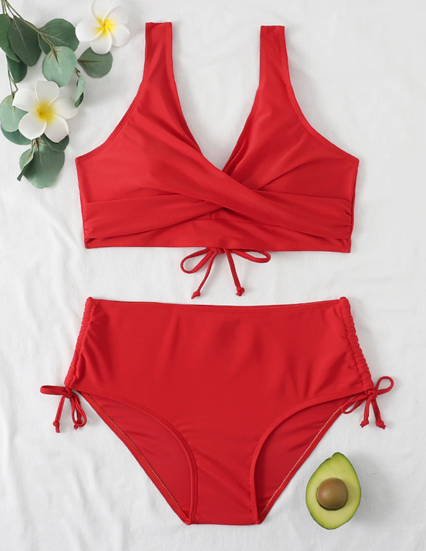 Maillot de bain rouge deux pièces avec haut croisé et culotte taille haute, décoré de fleurs blanches et d'un demi-avocat sur fond blanc.