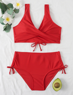 Maillot de bain rouge deux pièces avec haut croisé et culotte taille haute, décoré de fleurs blanches et d'un demi-avocat sur fond blanc.