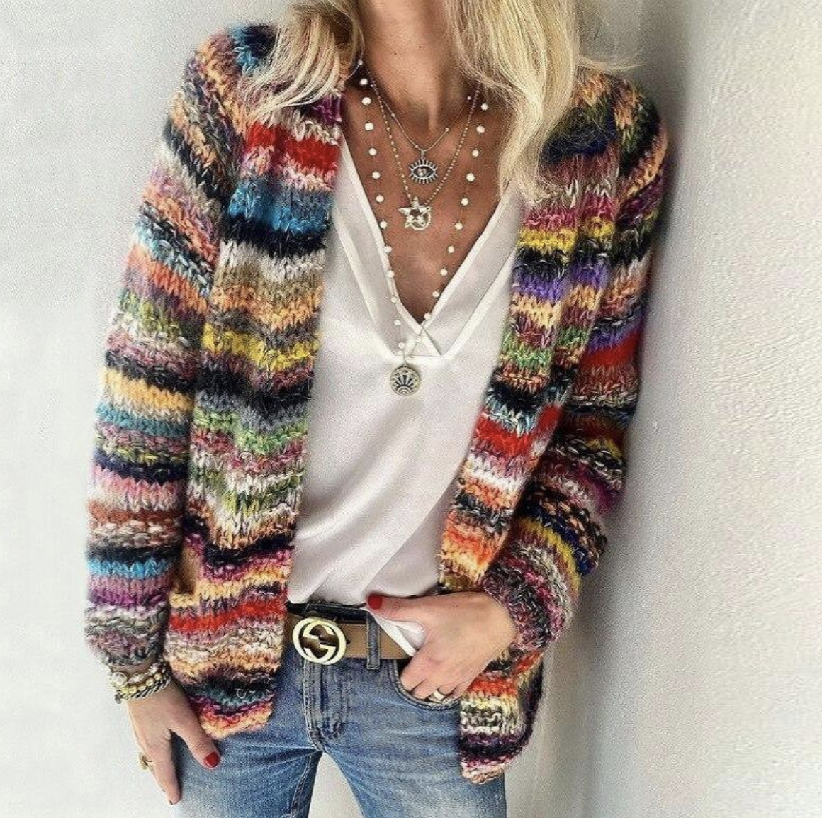 Femme portant un cardigan multicolore en laine, t-shirt blanc, jeans, colliers superposés et ceinture noire. Mode automne, style décontracté chic.