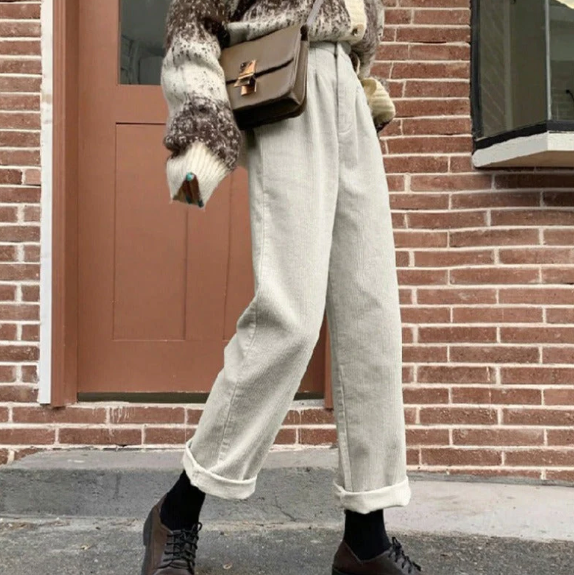 Pantalon beige ample en coton, style décontracté, porté avec un pull tricoté marron et des chaussures marron, devant une porte en brique.