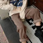 Personne assise portant un pantalon en velours côtelé marron, un sweat beige et des bottes noires, sur un sol en mosaïque noir et blanc.