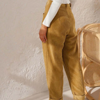 Pantalon en velours côtelé beige pour femme, style décontracté, avec pull blanc à manches longues, chaise en rotin en arrière-plan.