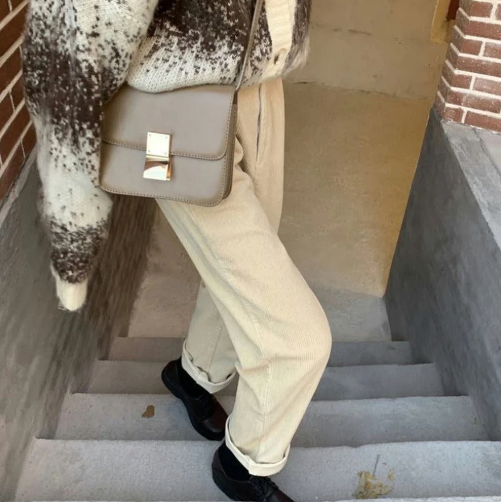 Personne montant des escaliers en pantalon beige, pull à motifs marron et blanc, sac à main taupe. Mode automne, style décontracté, accessoires tendance.