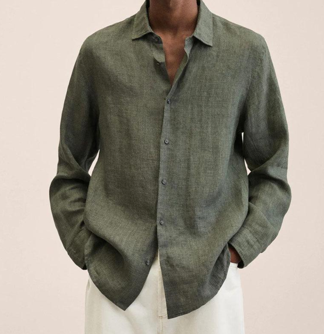 Chemise en lin vert olive pour homme, manches longues, col classique, boutons discrets, style décontracté, portée avec un pantalon blanc.