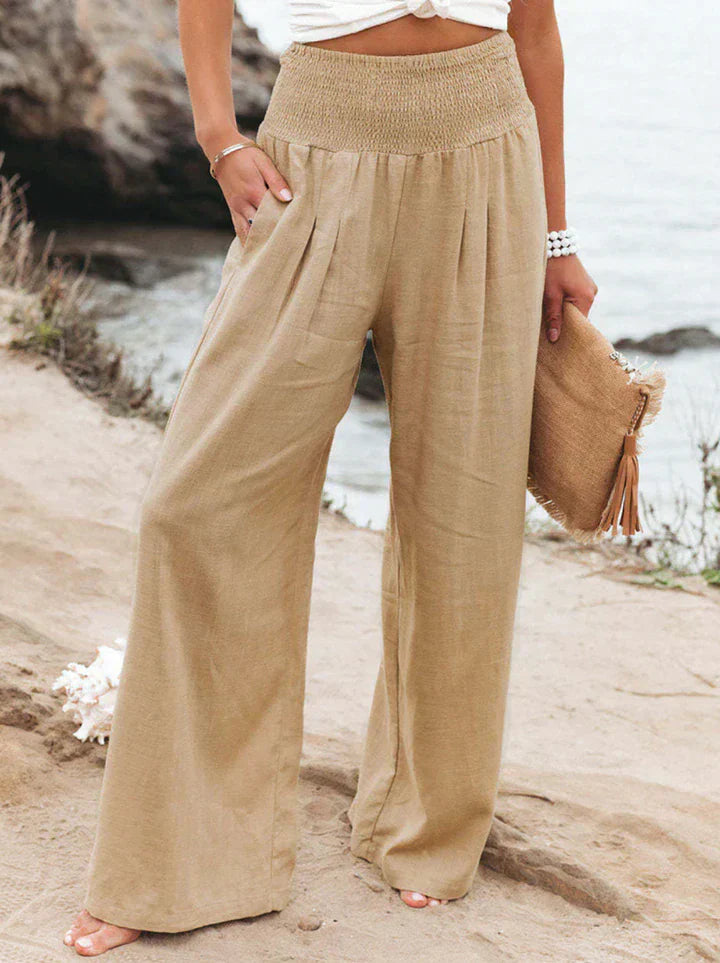 Pantalon large en lin beige pour femme, style décontracté, bord de mer. Mode estivale, tenue confortable, accessoire sac en paille.