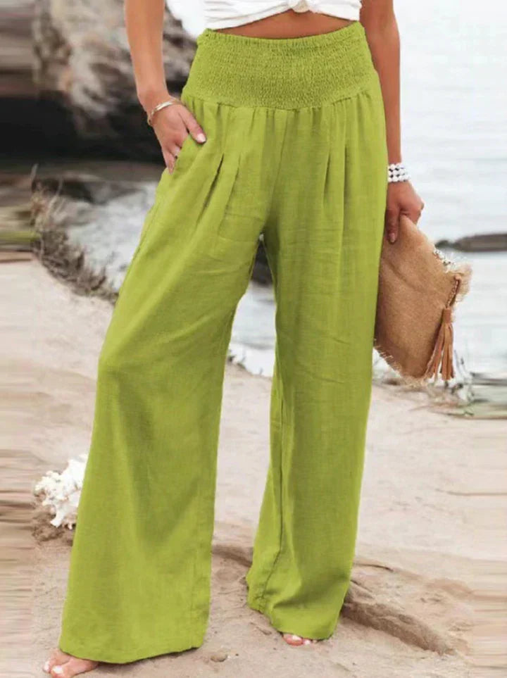 Pantalon large vert en lin pour femme, style décontracté, plage en arrière-plan, accessoire sac en paille, mode estivale tendance.