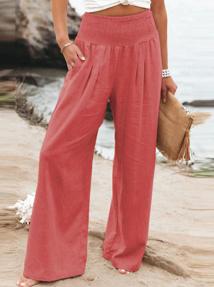 Pantalon large en lin rose pour femme, taille haute, avec poches, sur une plage. Mode estivale, tenue décontractée, style bohème chic.