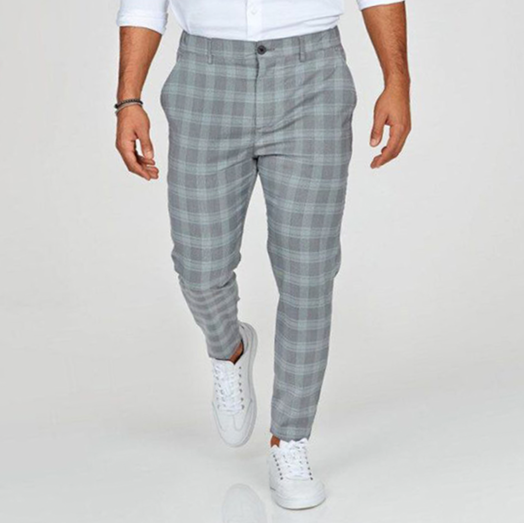 Pantalon à carreaux gris pour homme, style décontracté, porté avec chemise blanche et baskets blanches. Mode masculine élégante et moderne.