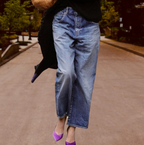 Jeans décontractés en denim bleu portés avec des talons violets sur une rue pavée, style urbain chic, mode automne, tendance casual.