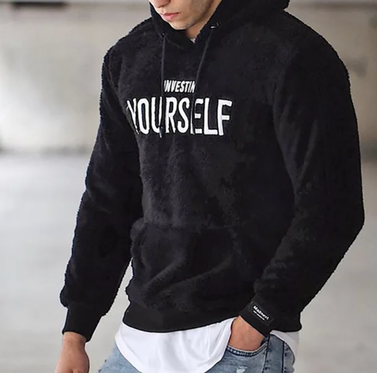 Homme portant un sweat à capuche noir avec inscription "Invest in Yourself", mode décontractée, style urbain, jeans, look moderne.