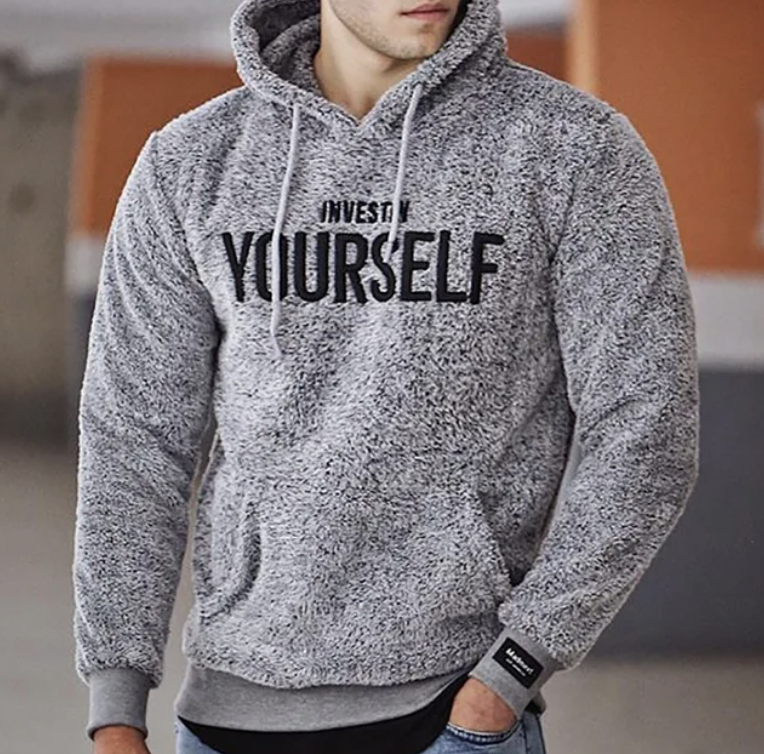 Homme portant un sweat à capuche gris texturé avec l'inscription "Invest in Yourself", mode décontractée, tendance automne-hiver, style urbain.