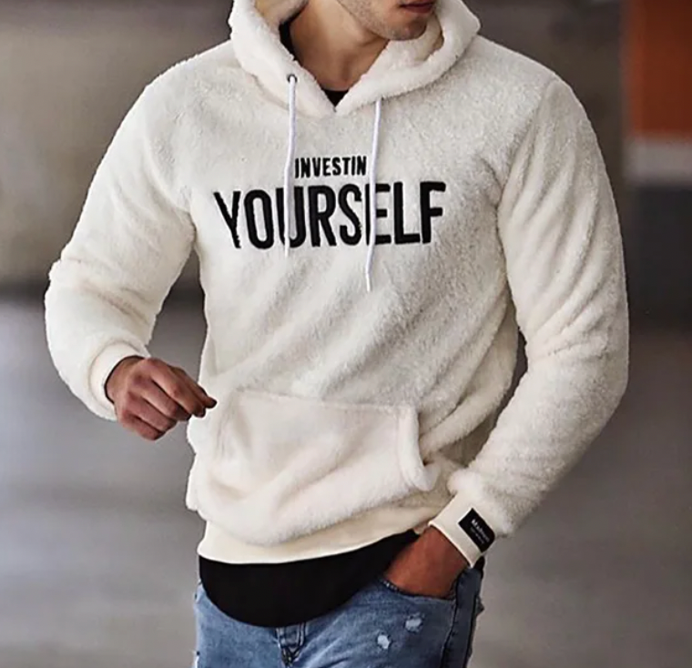 Homme portant un sweat à capuche blanc avec l'inscription "Invest in Yourself", mode décontractée, jeans déchirés, style urbain tendance.