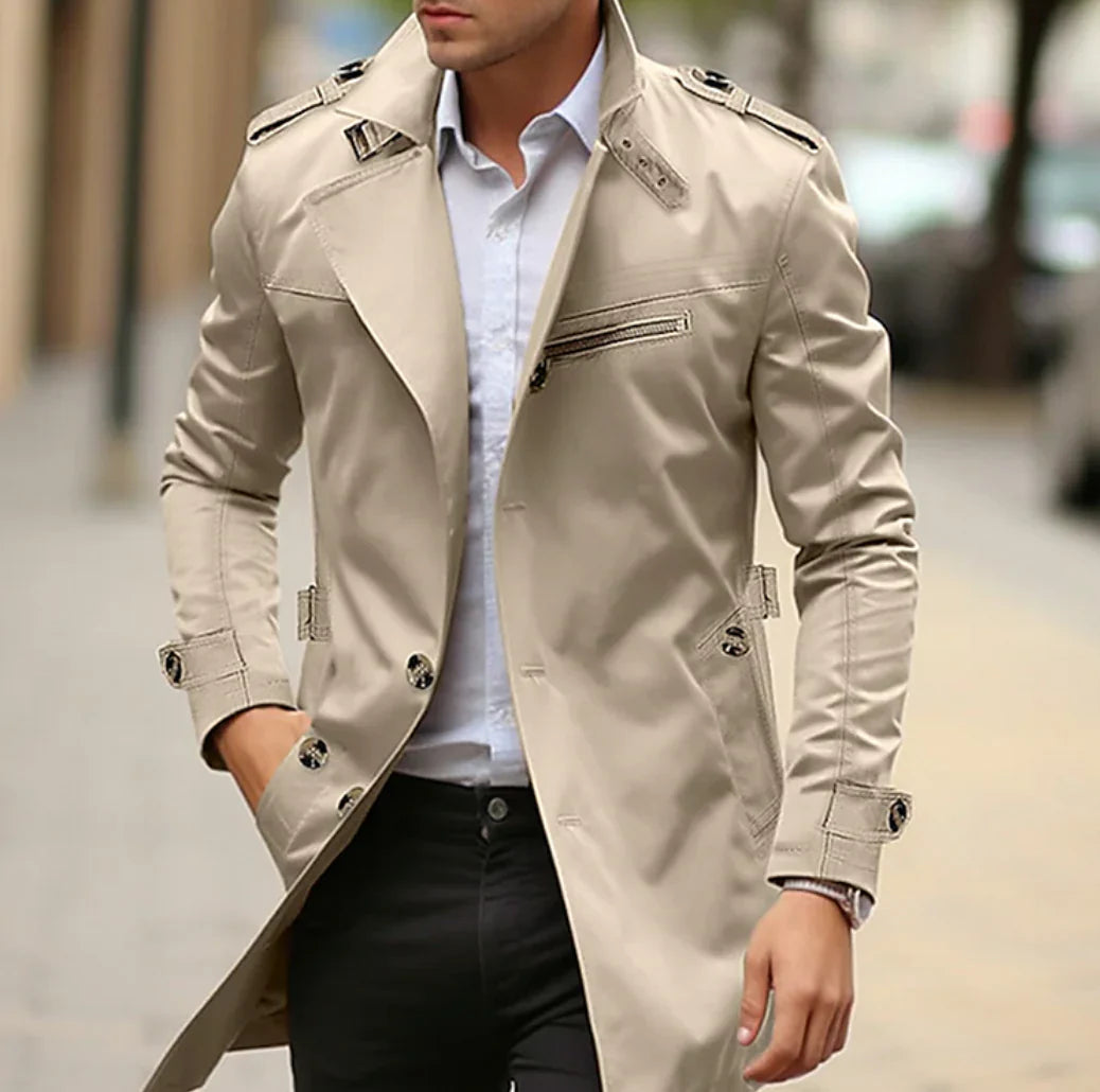Homme portant un trench-coat beige élégant, chemise blanche et pantalon noir, marchant en ville. Mode masculine, style urbain chic.