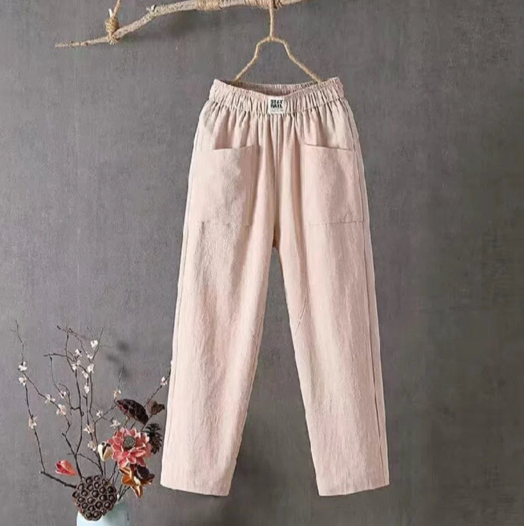 Pantalon en lin beige suspendu, style décontracté, avec poches avant. Décor floral en bas à gauche. Mode éco-responsable, tendance minimaliste.