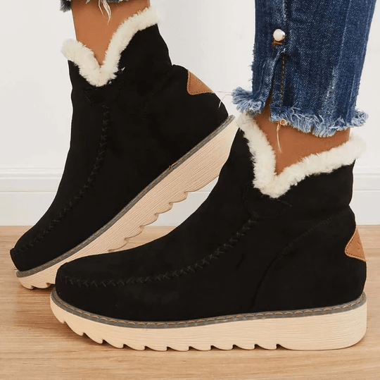 Bottes d'hiver noires en daim avec doublure en fourrure blanche, semelles crantées beiges, portées avec un jean déchiré. Mode féminine, chaussures chaudes.