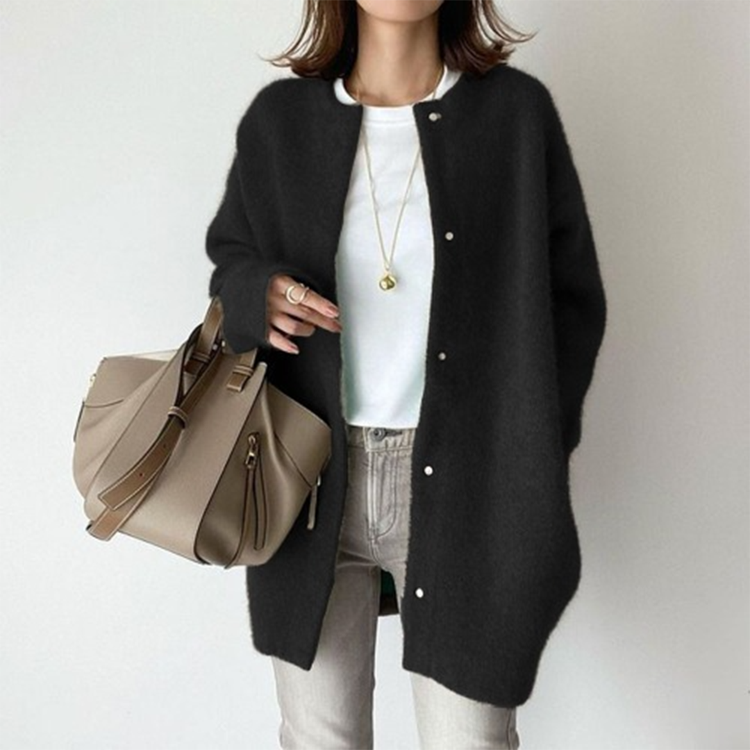 Femme portant un cardigan noir élégant, un sac à main beige moderne, un collier doré, et un jean gris. Mode automne chic et décontractée.