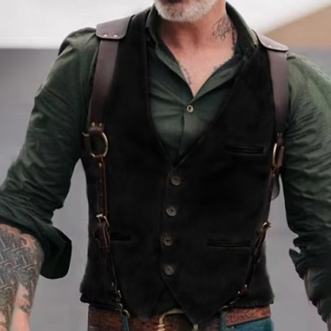 Gilet en cuir noir sur chemise verte, style vintage, avec bretelles en cuir marron. Homme barbu avec tatouages visibles sur le bras.
