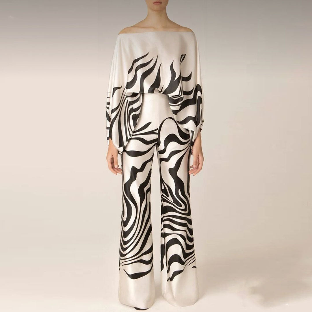 Combinaison élégante en satin blanc avec motifs noirs abstraits, manches longues, col bateau, pantalon large. Mode féminine chic et moderne.