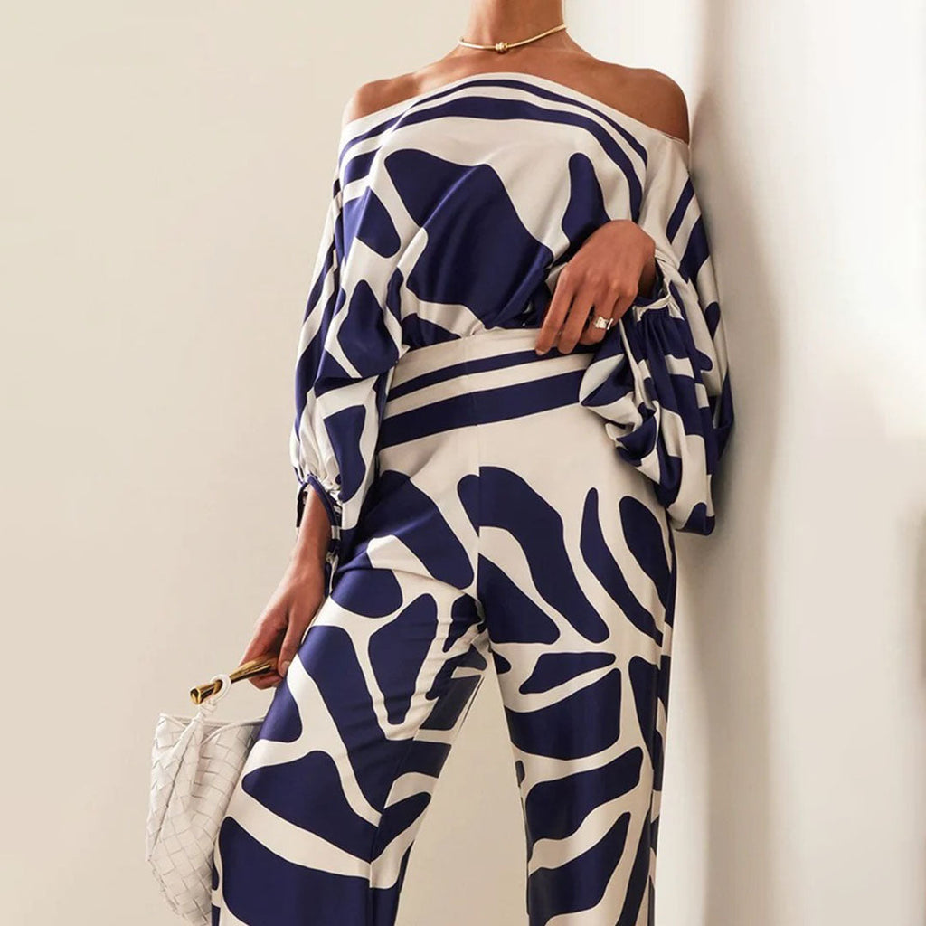 Robe élégante à motifs bleus et blancs, manches longues, épaules dénudées, accessoirisée d'un sac blanc. Mode chic et tendance.