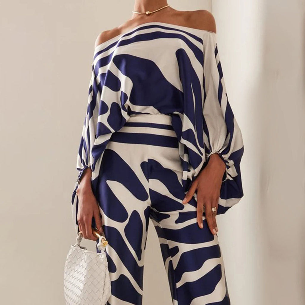 Tenue élégante à motifs bleus et blancs, avec haut asymétrique et pantalon assorti. Sac à main blanc tressé. Mode chic et moderne.
