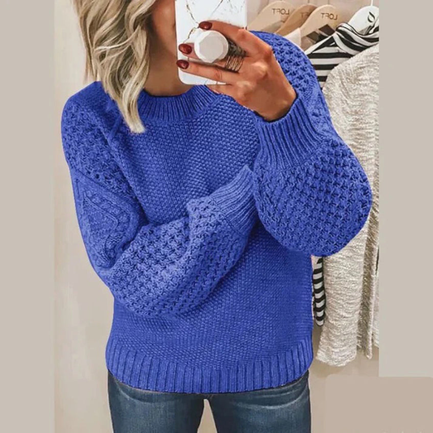 Femme portant un pull bleu en tricot texturé avec manches bouffantes, tenant un smartphone. Mode automne-hiver, style décontracté.