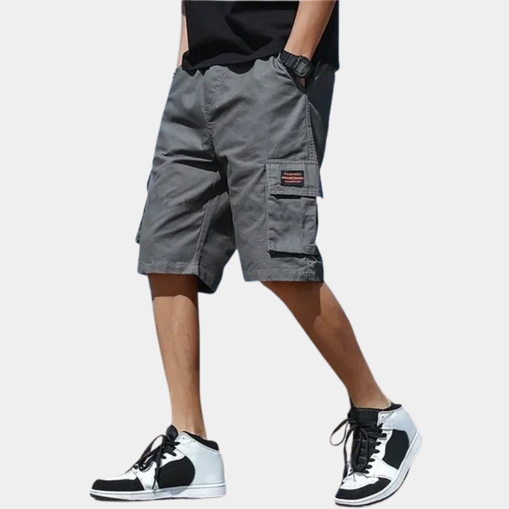 Homme portant un short cargo gris avec poches, t-shirt noir et baskets blanches et noires. Mode décontractée, style urbain, été.