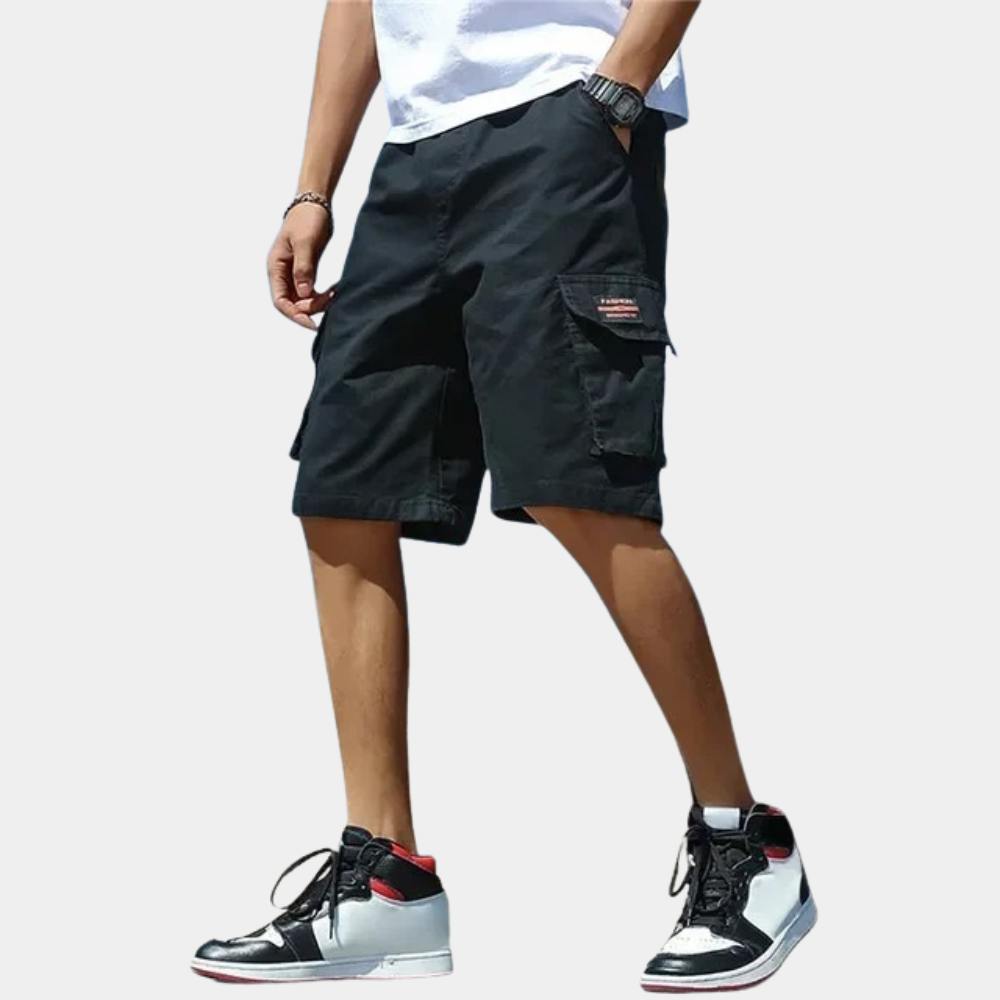 Homme portant un short cargo noir avec poches, t-shirt blanc et baskets montantes noires et blanches. Mode décontractée estivale tendance.