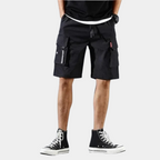 Short noir cargo pour homme avec poches multiples, porté avec des baskets montantes noires. Style décontracté et tendance pour l'été.