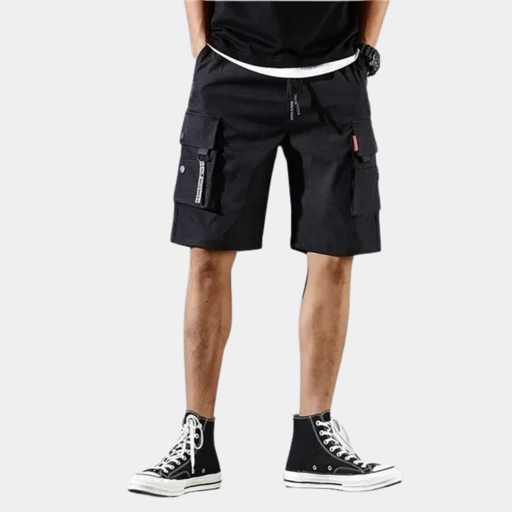 Short noir cargo pour homme avec poches multiples, porté avec des baskets montantes noires. Style décontracté et tendance pour l'été.
