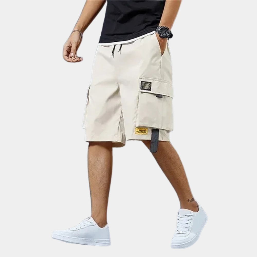 Homme portant un short cargo beige, t-shirt noir et baskets blanches. Mode décontractée, style urbain, tenue estivale pour homme.