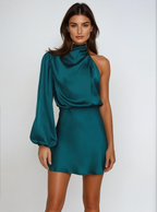 Robe satinée bleu-vert asymétrique à une manche, portée par une femme sur fond blanc. Mode élégante, tendance soirée, style moderne.