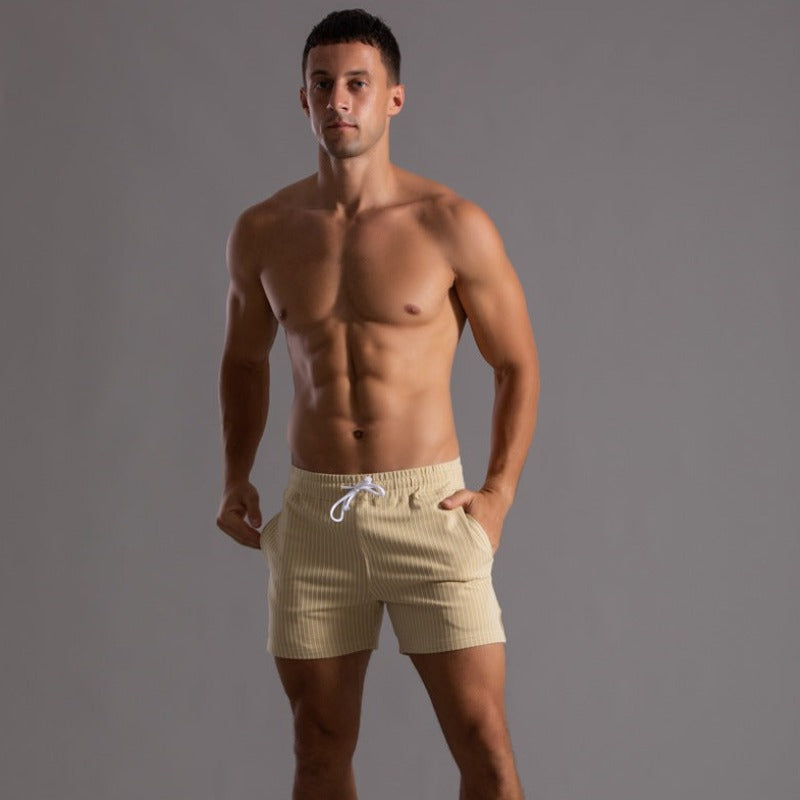 Homme musclé portant un short beige à cordon, pose sur fond gris. Mode masculine, vêtements d'été, style décontracté, fitness.