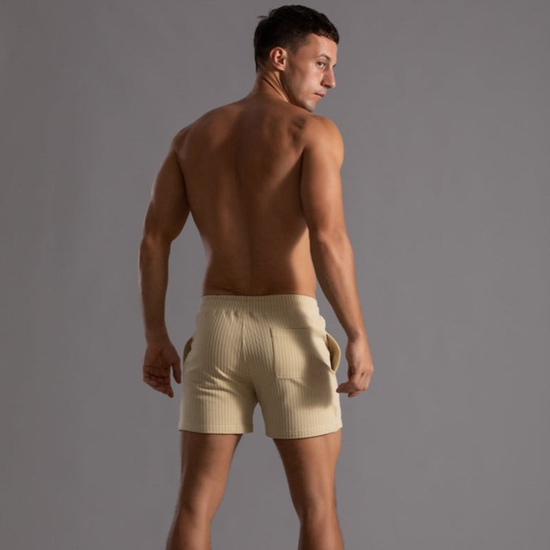 Homme en short beige côtelé, torse nu, de dos, sur fond gris. Mode masculine, tenue décontractée, style estival, vêtements modernes.