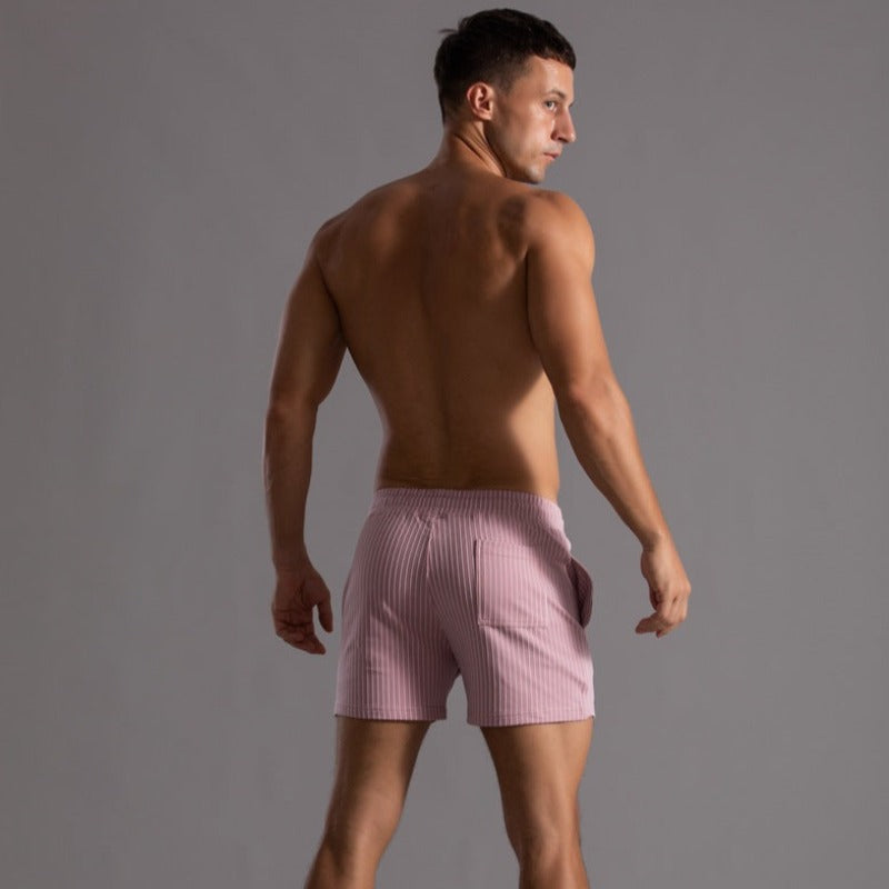 Homme en short rayé rose, torse nu, de dos, sur fond gris. Mode masculine, vêtements d'été, style décontracté, tendance 2023.