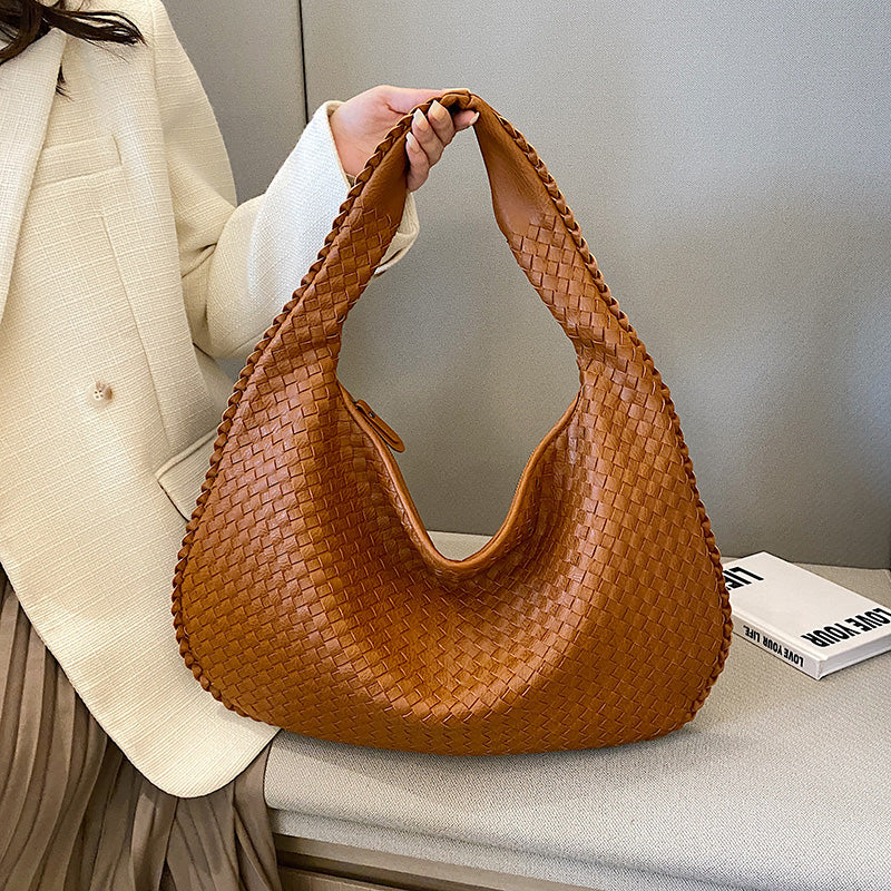 Sac à main en cuir tressé marron, porté par une personne en manteau beige. Accessoire mode élégant, tendance automne, style chic et sophistiqué.