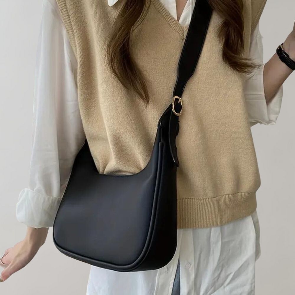 Sac à bandoulière noir élégant porté par une femme en pull beige et chemise blanche, accessoire mode tendance pour un look chic et moderne.