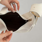 Sac à main blanc ouvert avec doublure noire, fermetures éclair dorées, tenu par des mains féminines. Accessoire mode élégant et tendance.