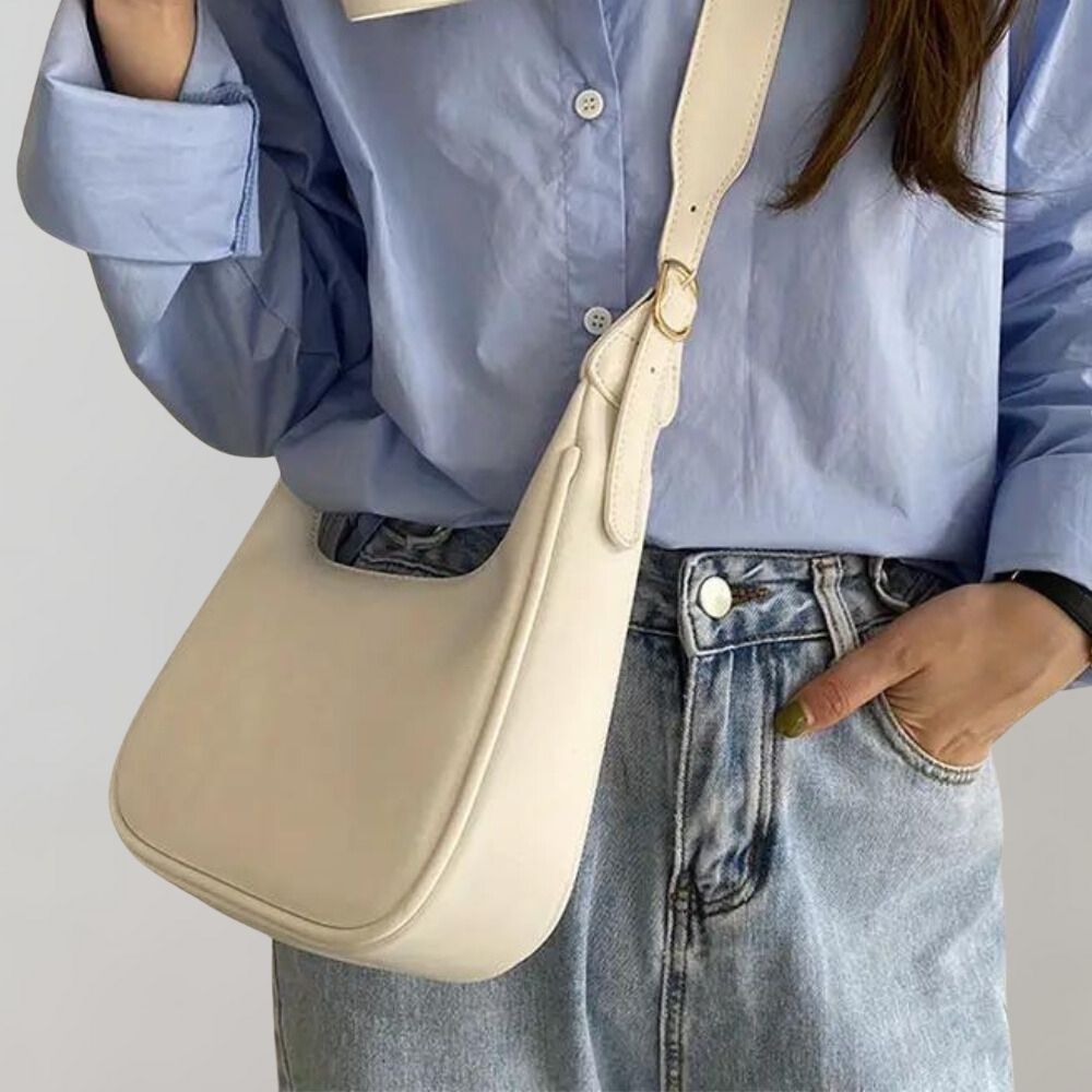 Femme portant un sac à bandoulière beige élégant, chemise bleue et jean décontracté. Mode féminine, accessoires tendance, style urbain chic.