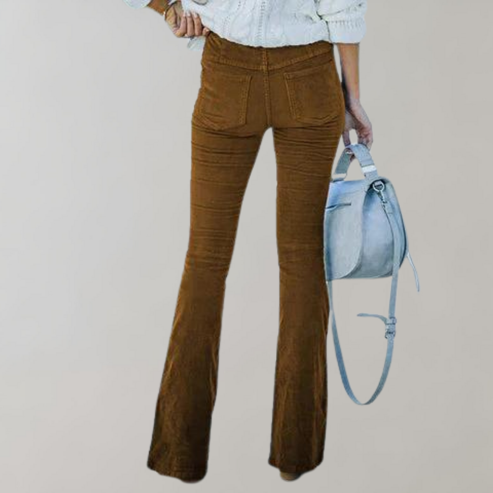 Femme portant un pantalon évasé marron, chemise blanche, tenant un sac à main gris. Mode automne, style rétro, tenue décontractée.