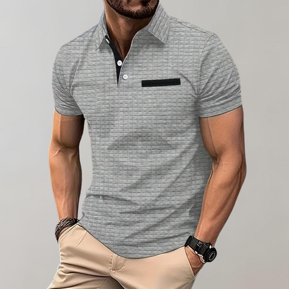Homme portant un polo gris texturé avec poche noire, manches courtes, associé à un pantalon beige. Mode masculine élégante et décontractée.