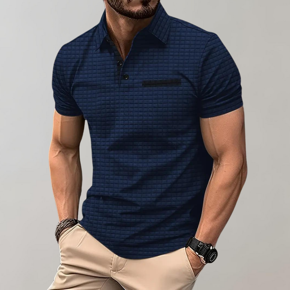 Homme portant un polo bleu à motifs, manches courtes, avec pantalon beige. Style décontracté, montre noire, bracelet au poignet. Mode masculine élégante.