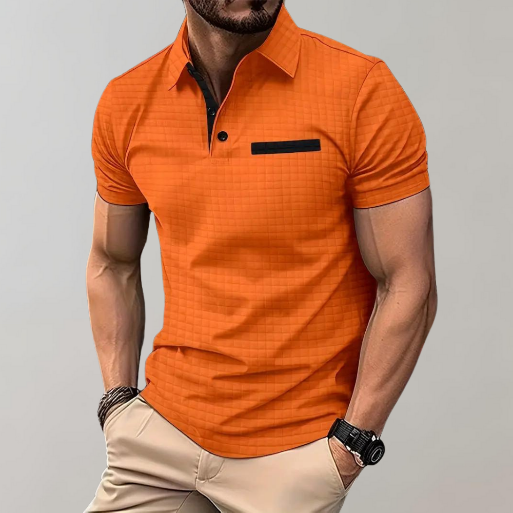Homme portant un polo orange à manches courtes avec poche noire, style décontracté, sur fond gris. Mode masculine, tenue estivale élégante.