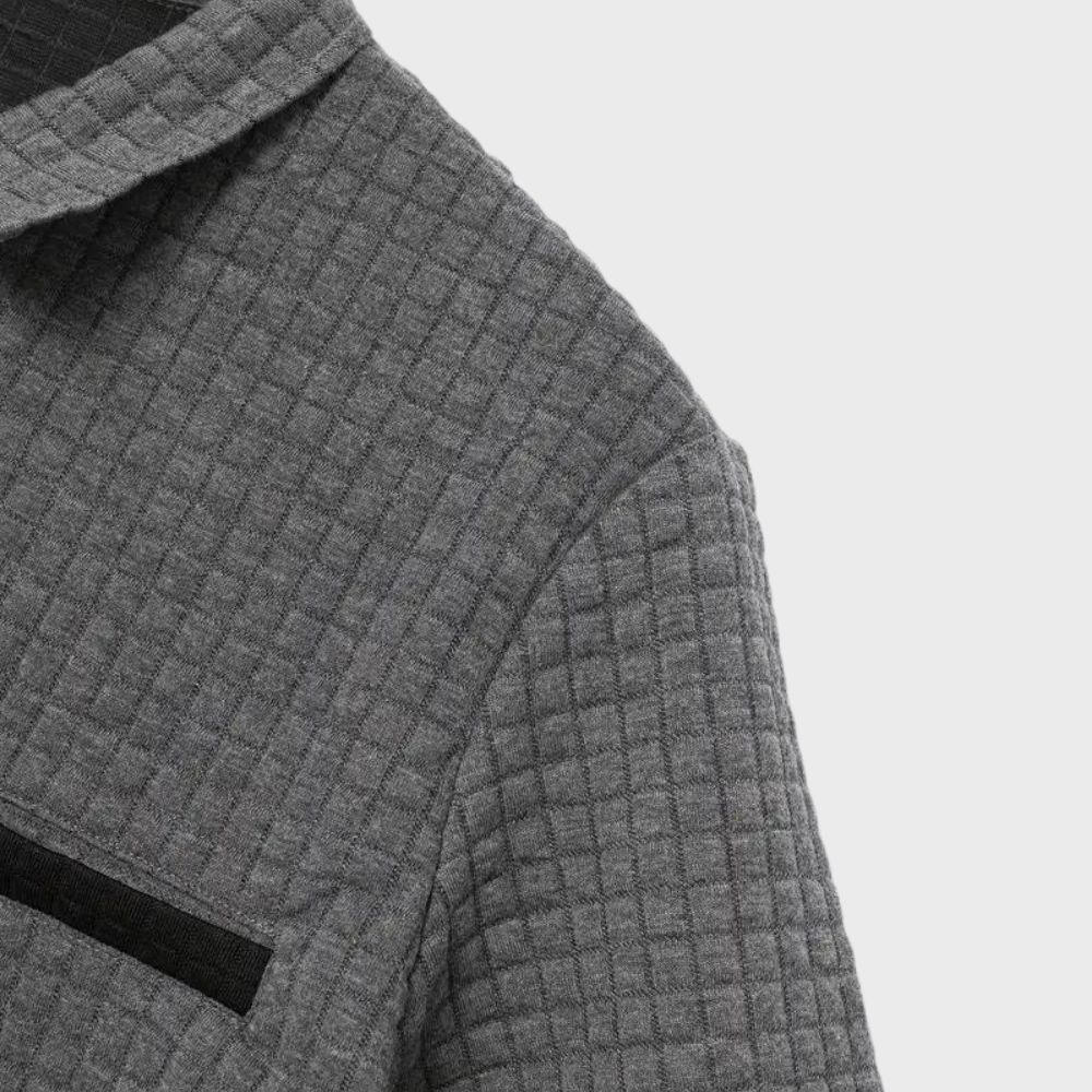 Veste en laine grise à motif quadrillé, col classique, poche poitrine noire, style élégant et moderne, mode automne-hiver.